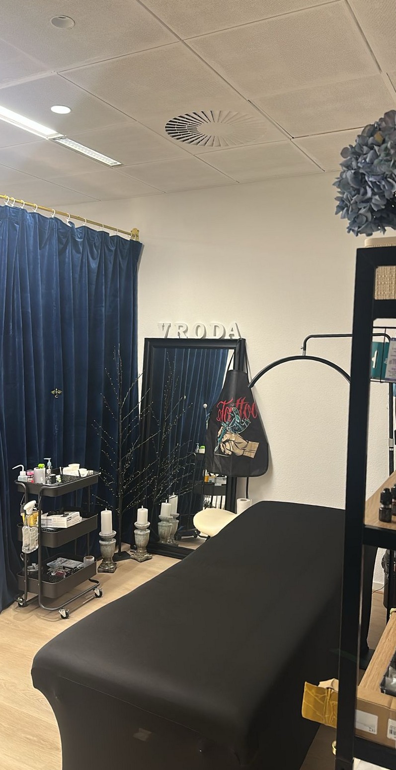 Behandelkamer van Vroda met een zwarte behandelstoel, een trolley, blauwe gordijnen en VRODA op de wand