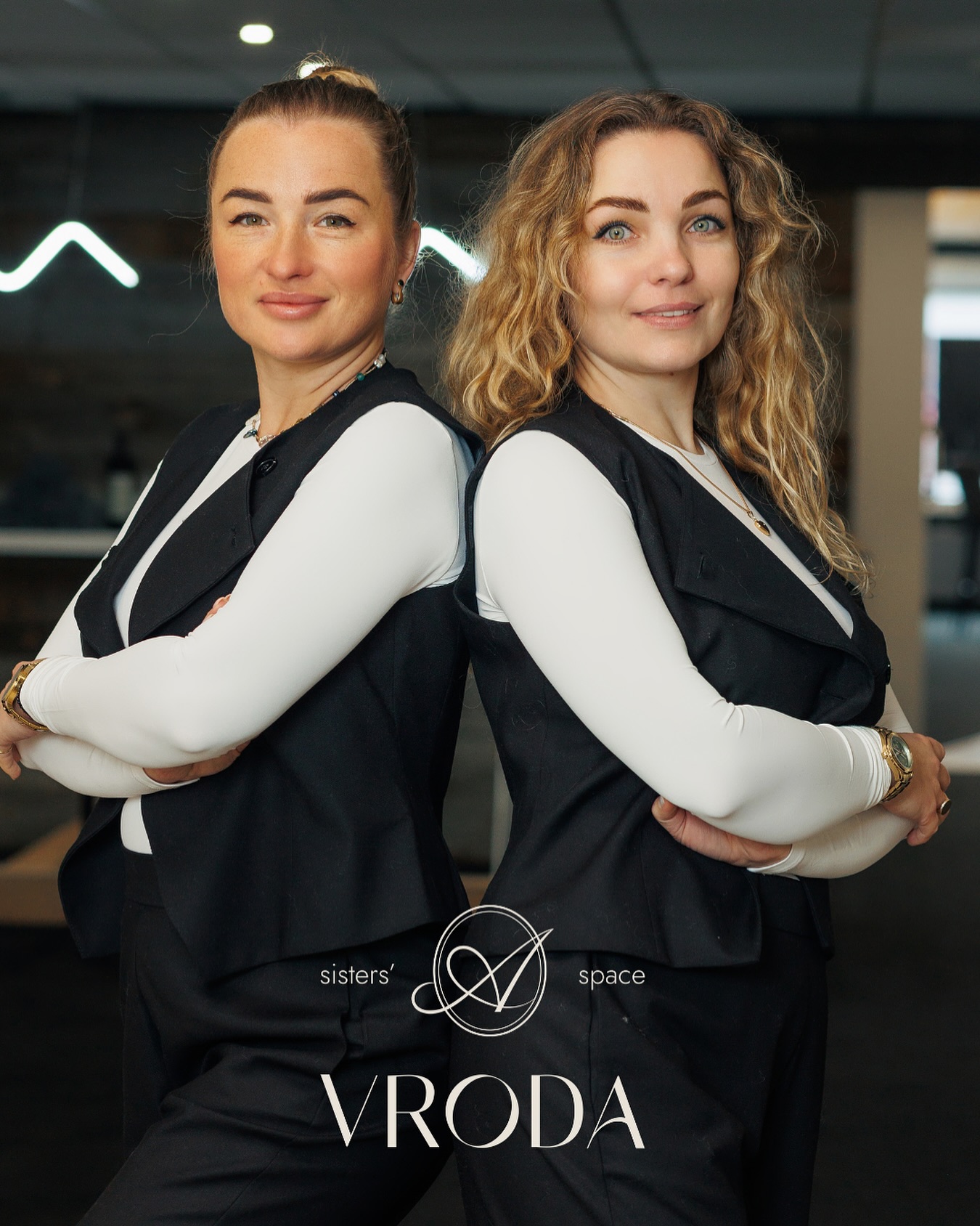 Twee vrouwen van Vroda in zwarte gilets, rug aan rug met de armen over elkaar, met het Vroda sisters' space logo
